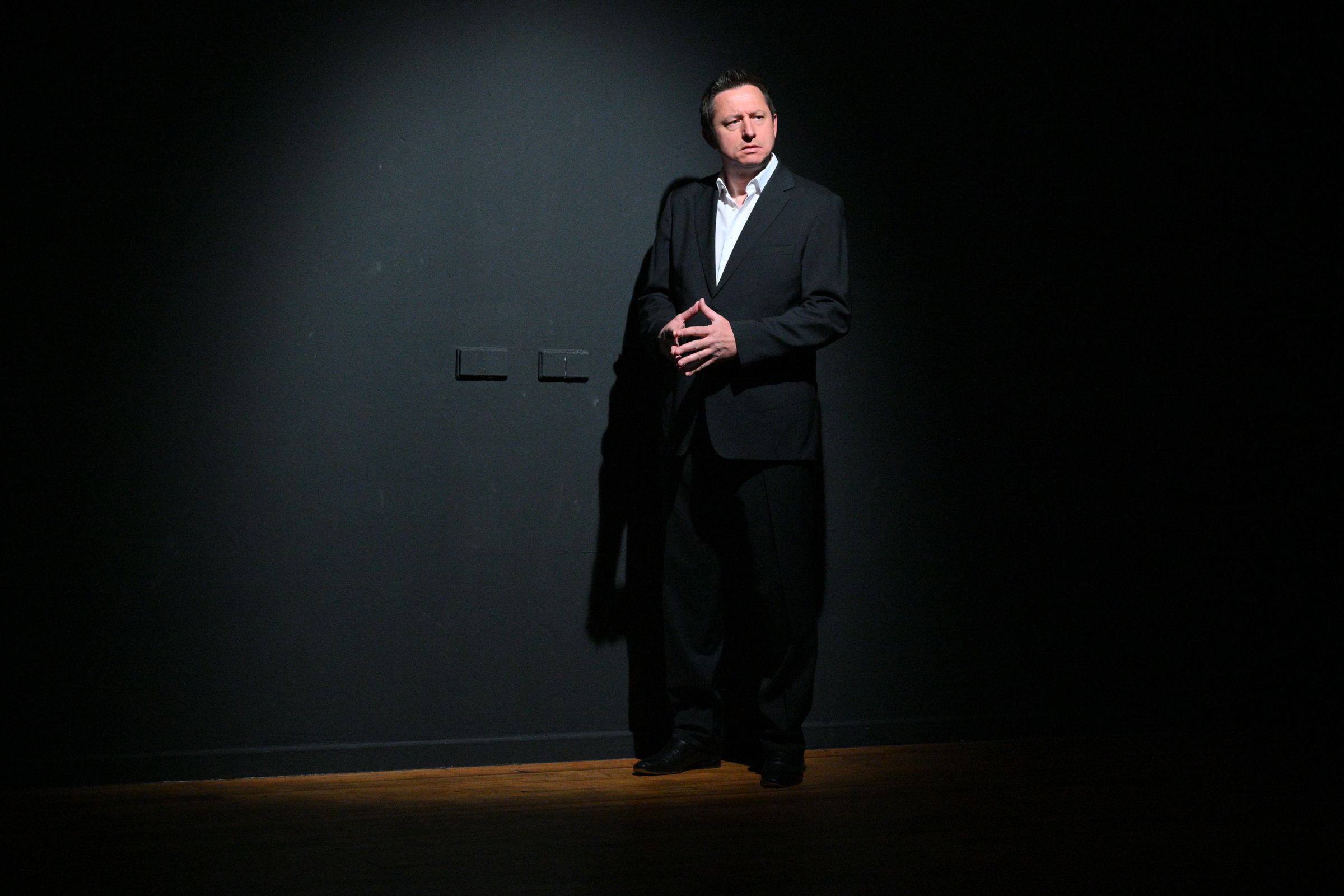 Alexander Nikolaus Stelzer im Anzug auf einer Bühne, im Scheinwerferlicht vor einer dunklen Wand